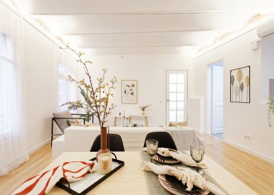 Mesa puesta con vajilla y flores en comedor de planta abierta.